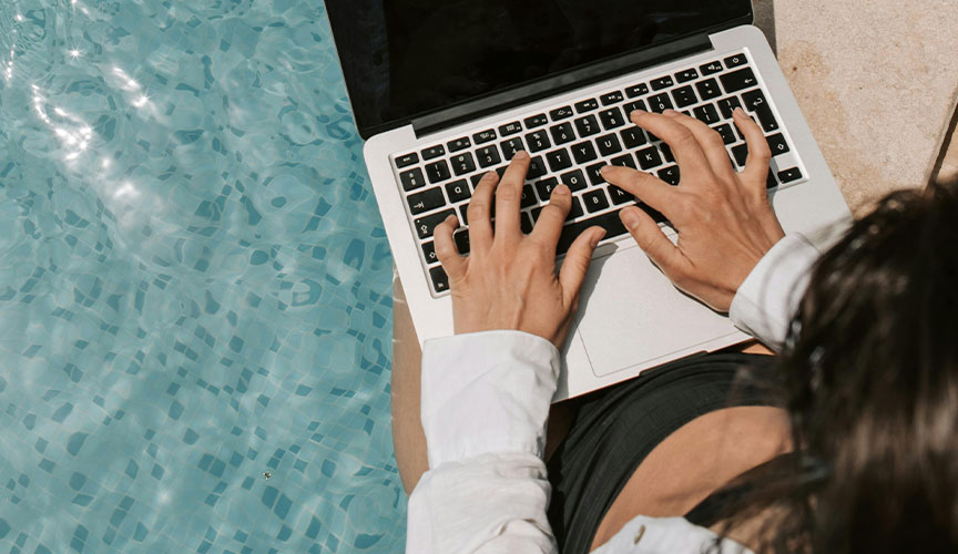 Photo of a person sitting by the poolside with his/her laptop